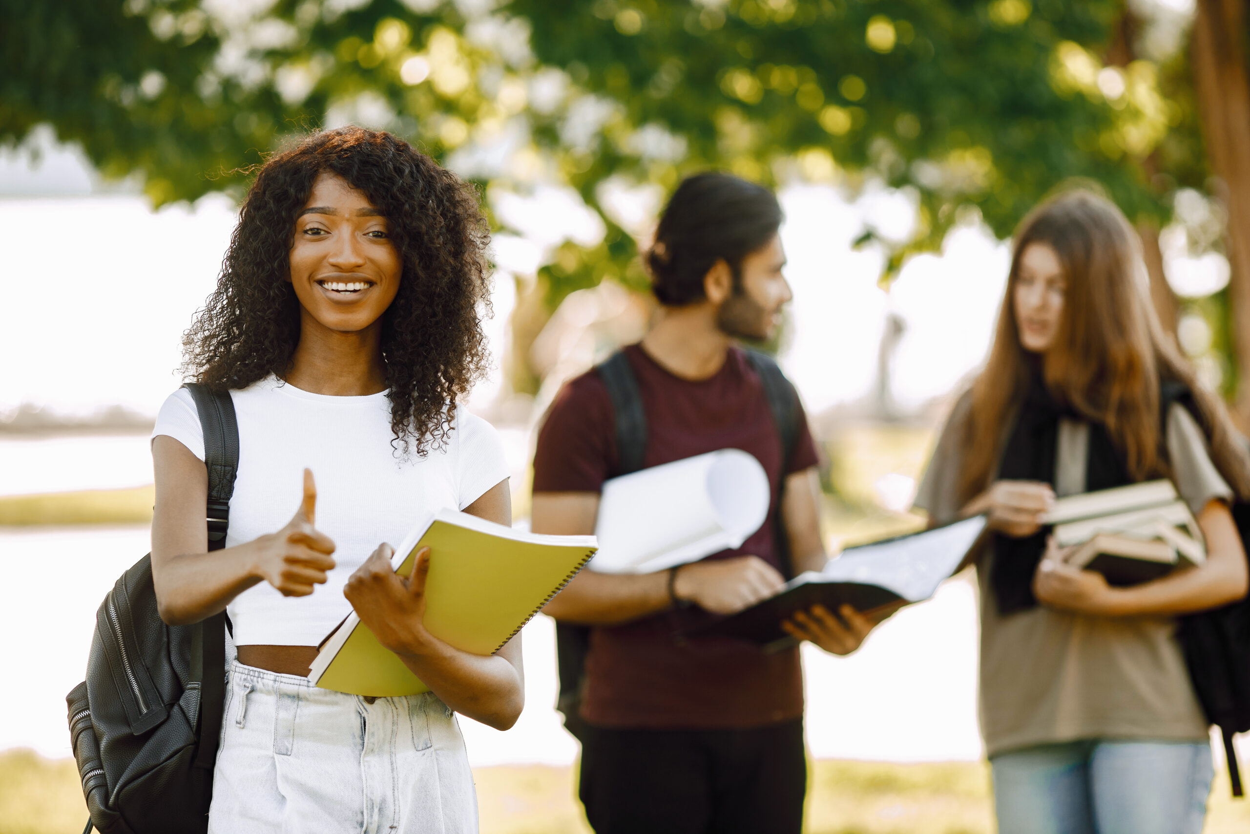 three international students standing in a park and holding a bo